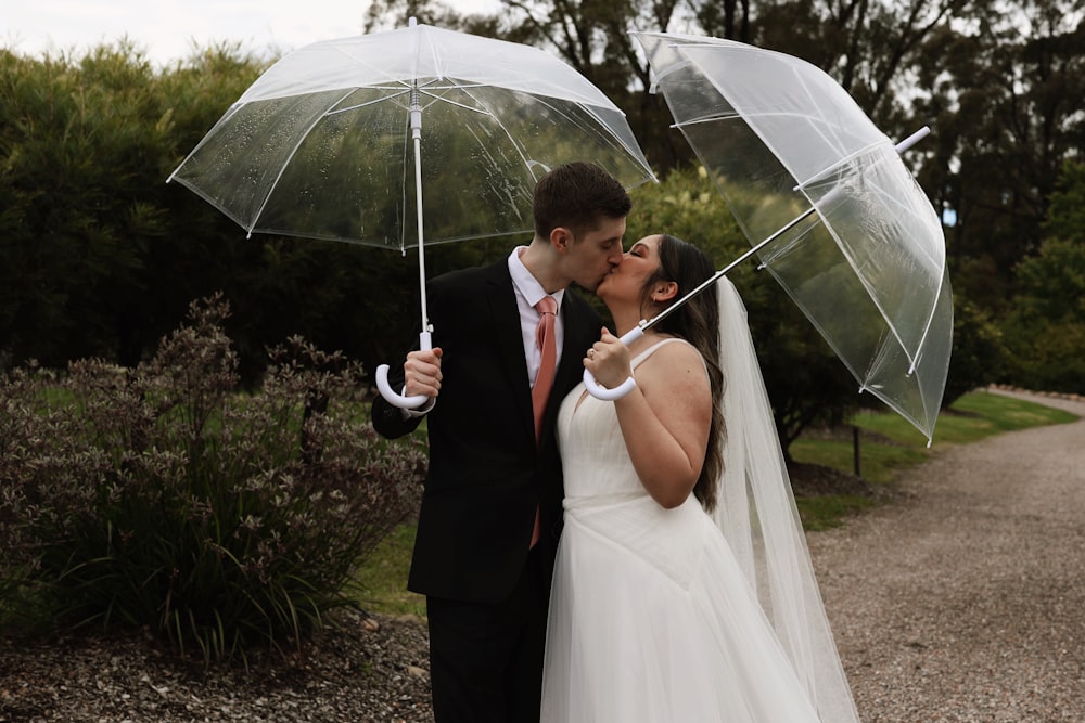 a bride and groom kissing under clear umbrellas