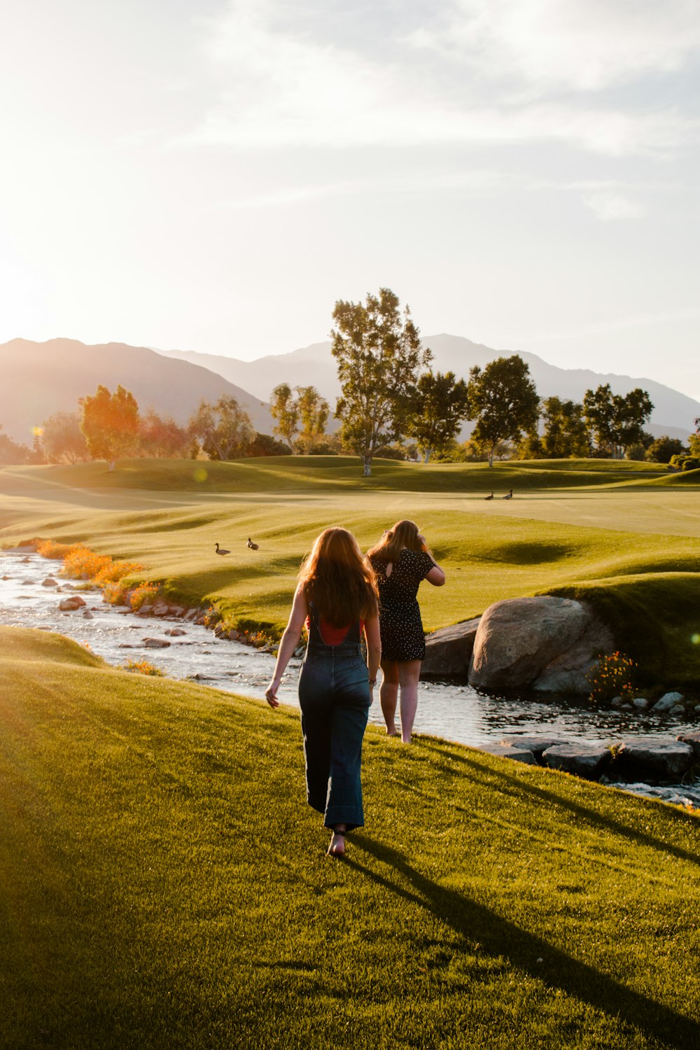 a couple of women walking across a lush green field