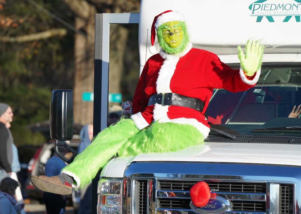 a man dressed as grinen sitting on the hood of a truck