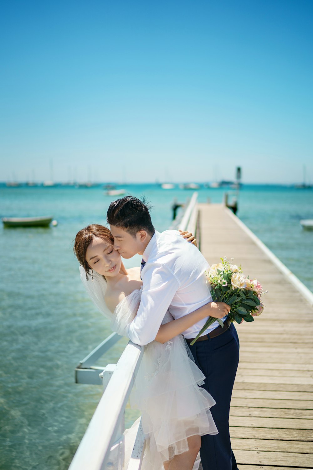 a bride and groom embracing on a pier