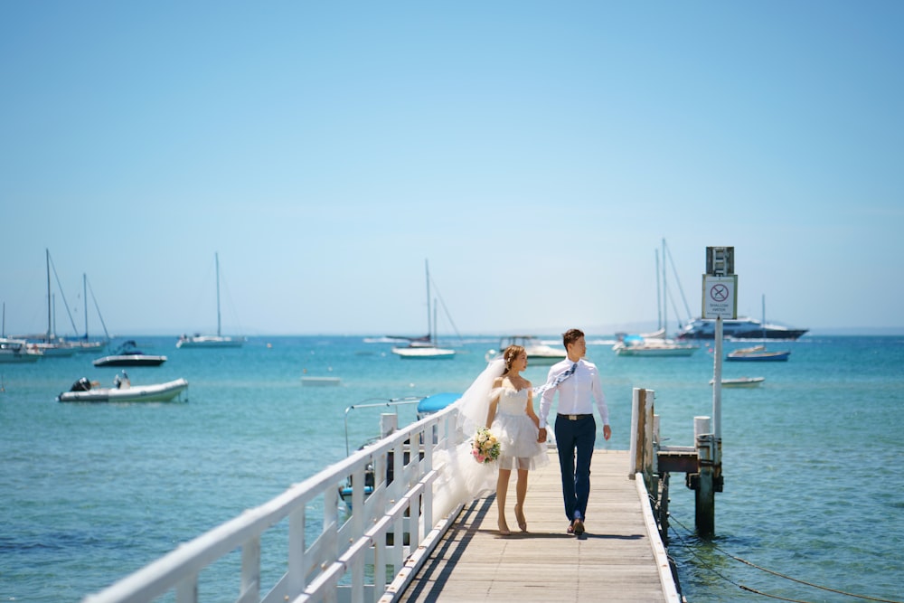 a bride and groom walking down a pier towards the ocean