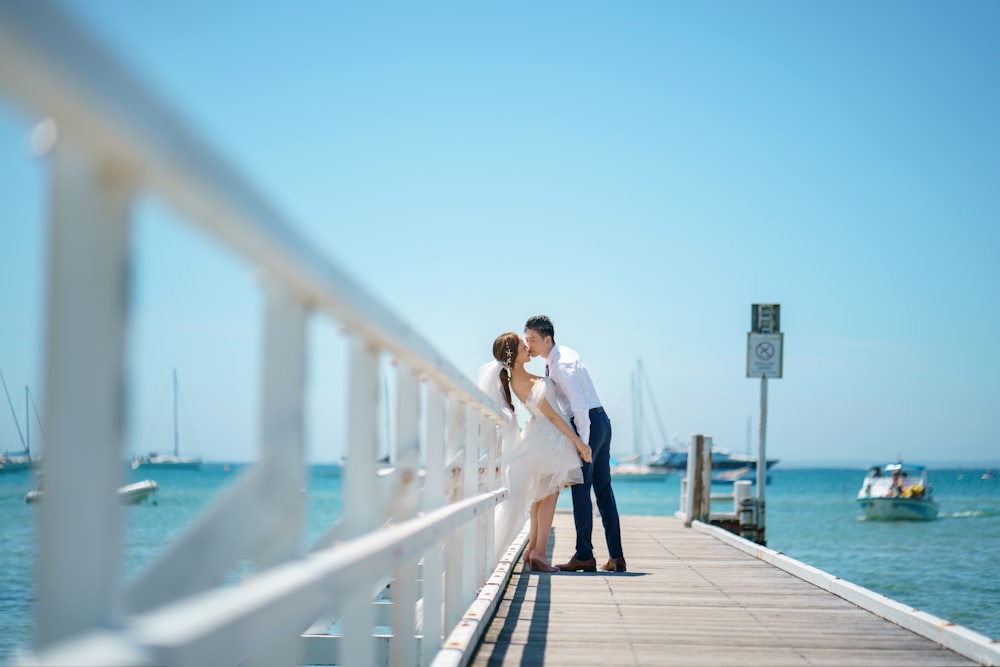 a bride and groom kissing on a pier