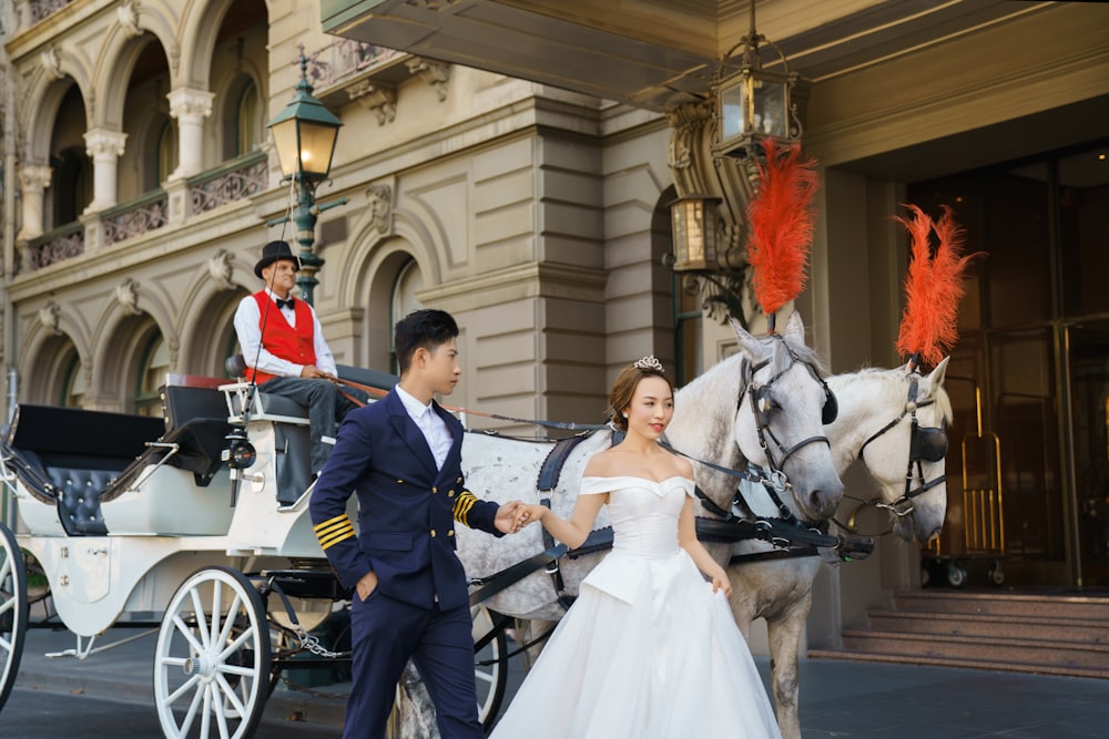 a man and a woman in a wedding dress are walking with a horse drawn carriage