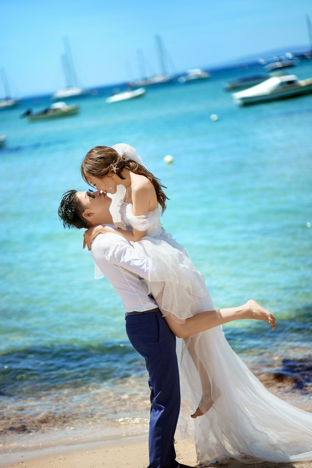 a bride and groom kissing on the beach