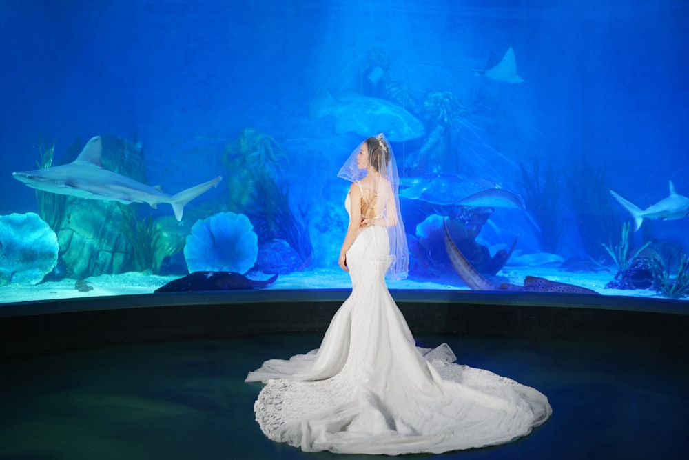 a woman in a wedding dress standing in front of a fish tank