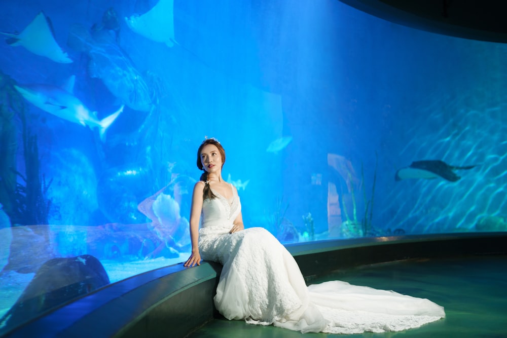 a woman in a white dress sitting on a bench in front of a fish tank