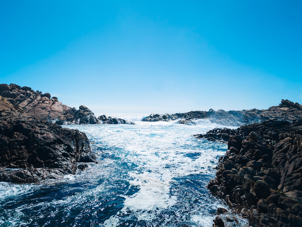 a body of water surrounded by rocks under a blue sky