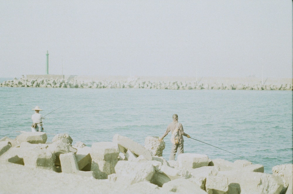 a man standing on a rocky shore next to a body of water