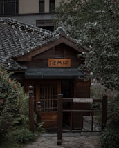A serene Japanese-style wooden house entrance surrounded by seasonal greenery.