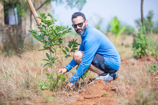 a man kneeling down next to a small tree