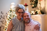 a man and a woman pose for a picture in front of a christmas tree