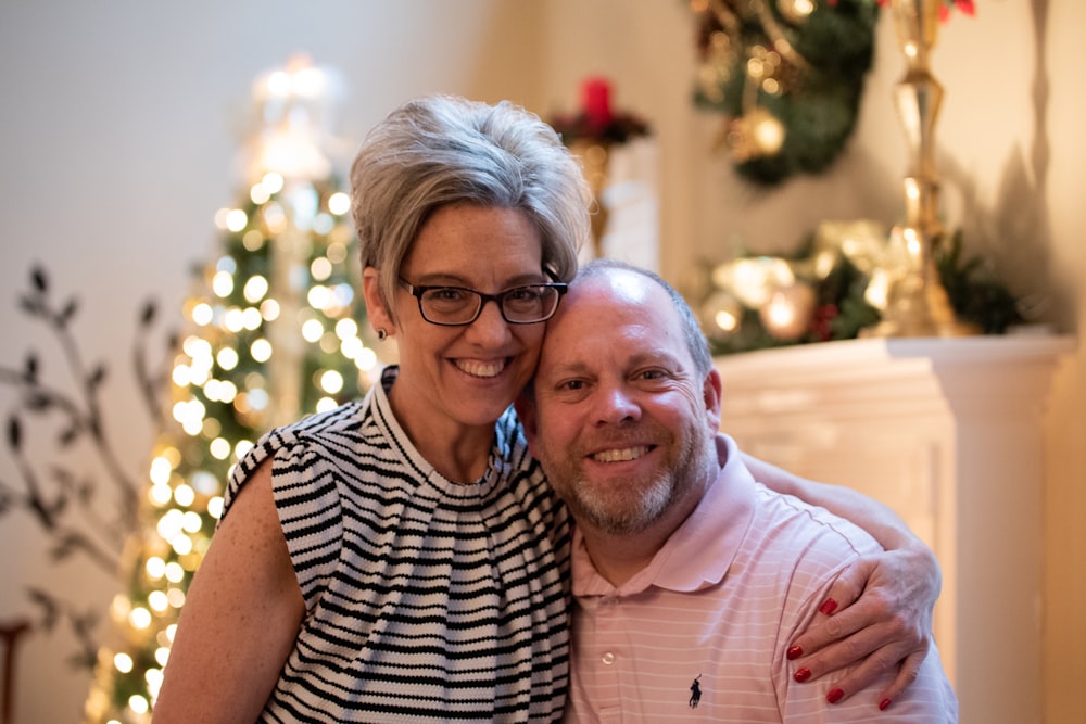a man and a woman pose for a picture in front of a christmas tree