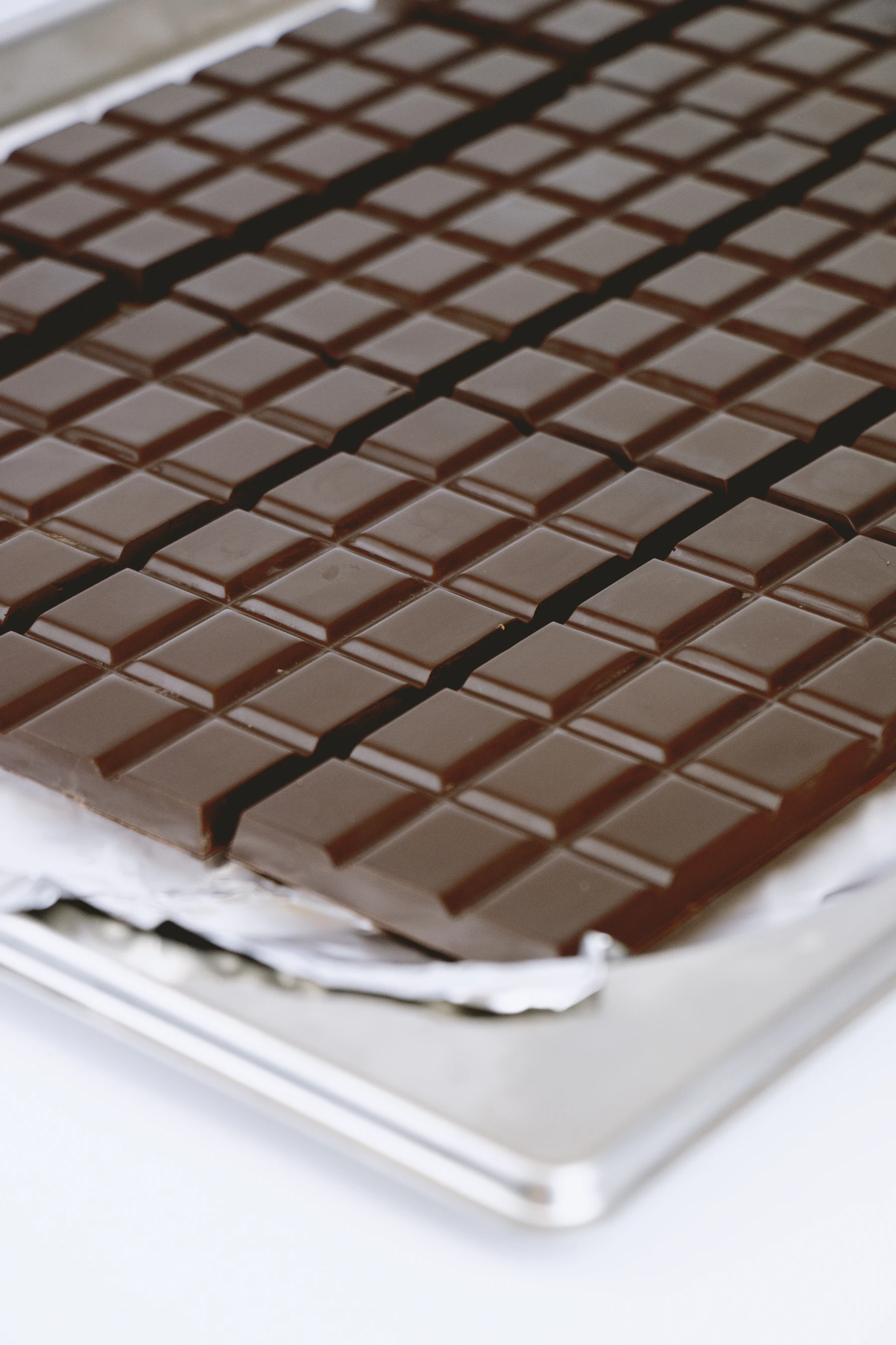 A large glossy dark chocolate slab scored into squares on a sheet tray