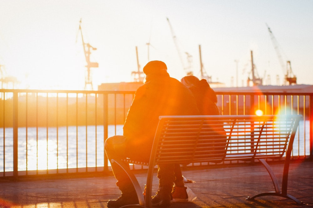 two people sitting on a bench next to a body of water
