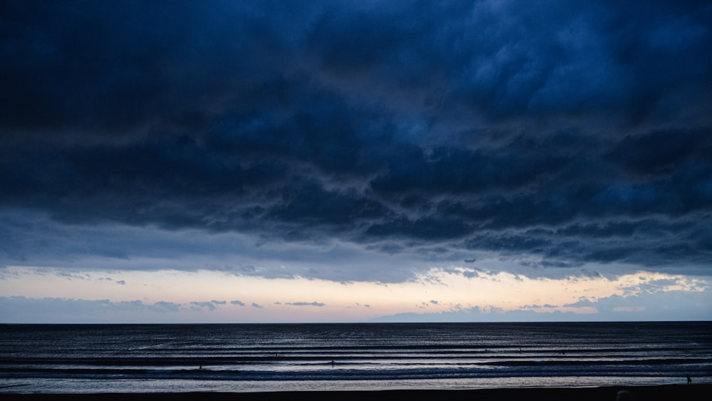 a couple of people walking on a beach under a cloudy sky