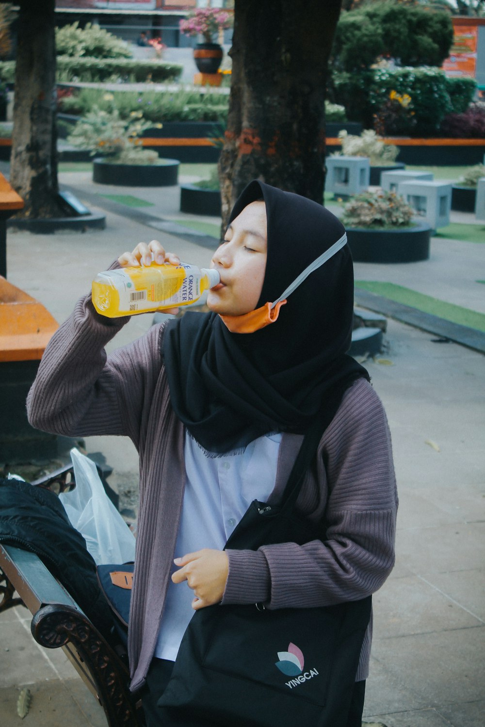 a woman sitting on a bench drinking from a bottle