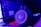 A pair of gaming headphones sits in front of a laptop displaying a chat application. The scene is bathed in a combination of blue and purple lighting, giving a high-tech and immersive atmosphere. The headphones have glowing red accents, enhancing the futuristic vibe.