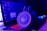 A pair of gaming headphones sits in front of a laptop displaying a chat application. The scene is bathed in a combination of blue and purple lighting, giving a high-tech and immersive atmosphere. The headphones have glowing red accents, enhancing the futuristic vibe.