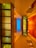A symmetrical interior view featuring modern architectural elements with a strong emphasis on geometric shapes. The ceiling and walls are illuminated by warm, ambient lighting, casting an inviting glow. Glass partitions with metal frames create a contrast with wooden panels that add a rich texture. A central pane of blue-tinted glass draws the eye upwards, providing a cool contrast.