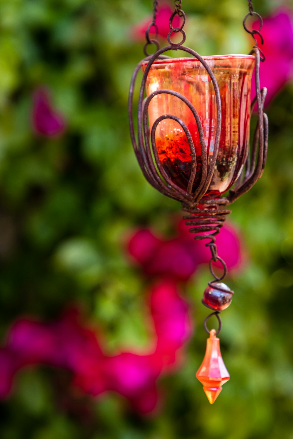a glass hanging from a chain with flowers in the background