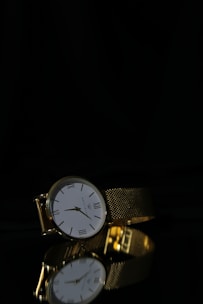 An elegant chronograph watch resting on a glossy black surface with hints of gold reflections.