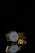 A luxurious gold wristwatch with a white face and Roman numerals is positioned on a reflective black surface. The watch features an intricate gold mesh strap and the reflection of the watch is clearly visible below it.