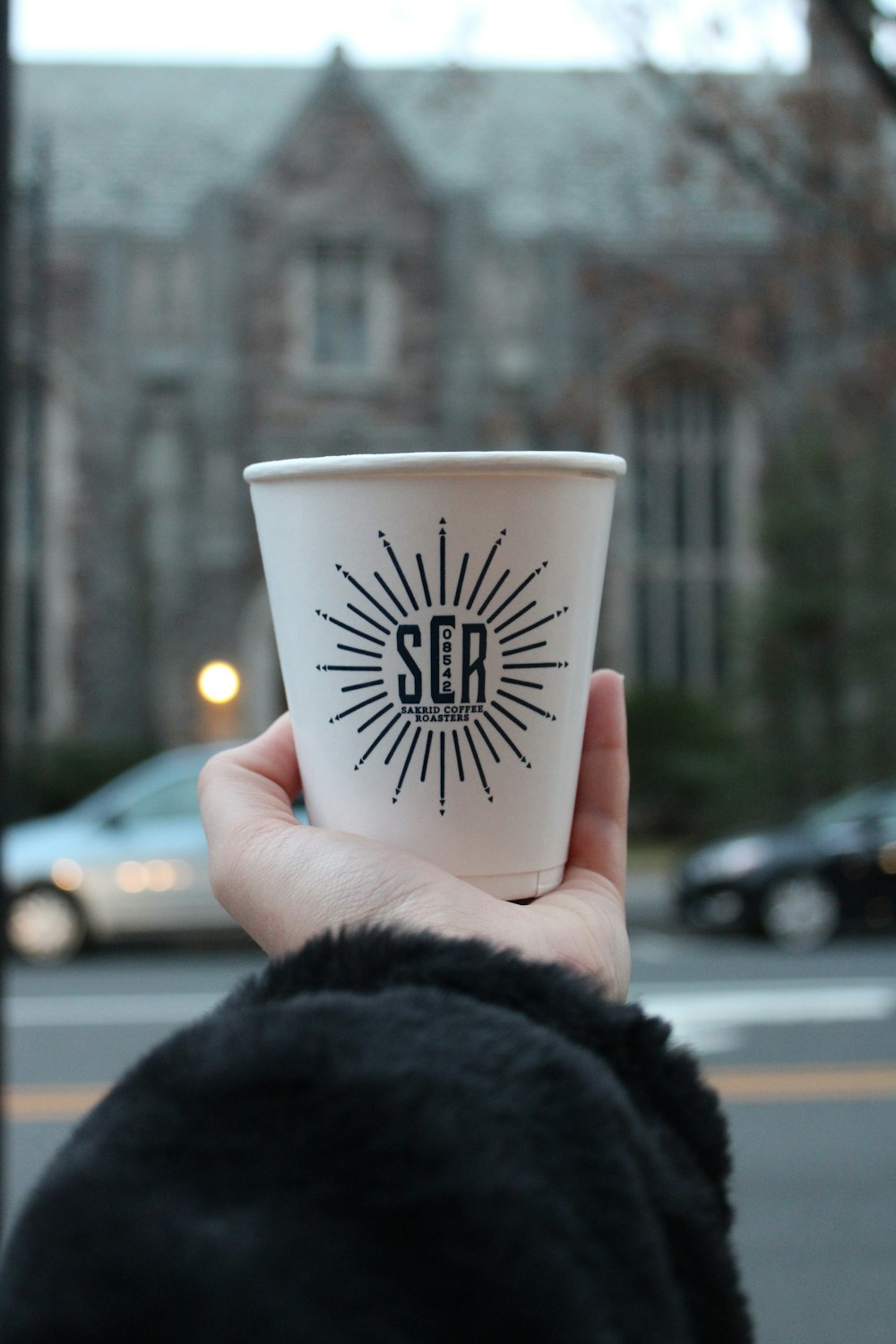 a person holding a cup of coffee in front of a building
