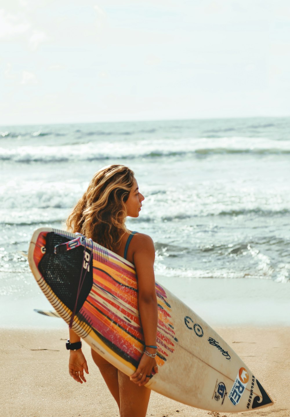 a woman holding a surfboard on top of a sandy beach