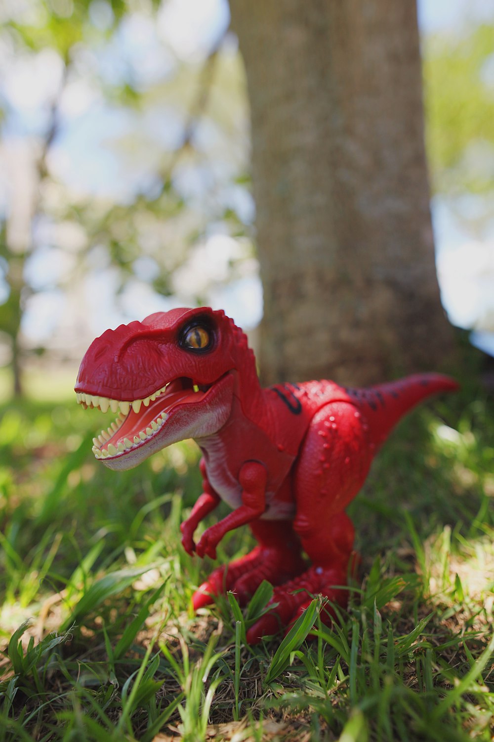 um brinquedo t - rex em pé na grama ao lado de uma árvore