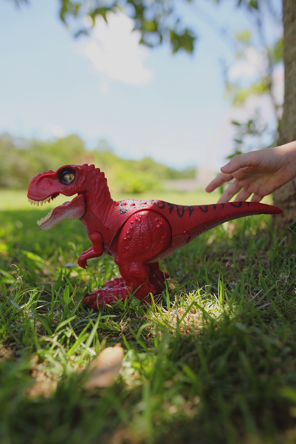 a red toy dinosaur in the grass next to a tree