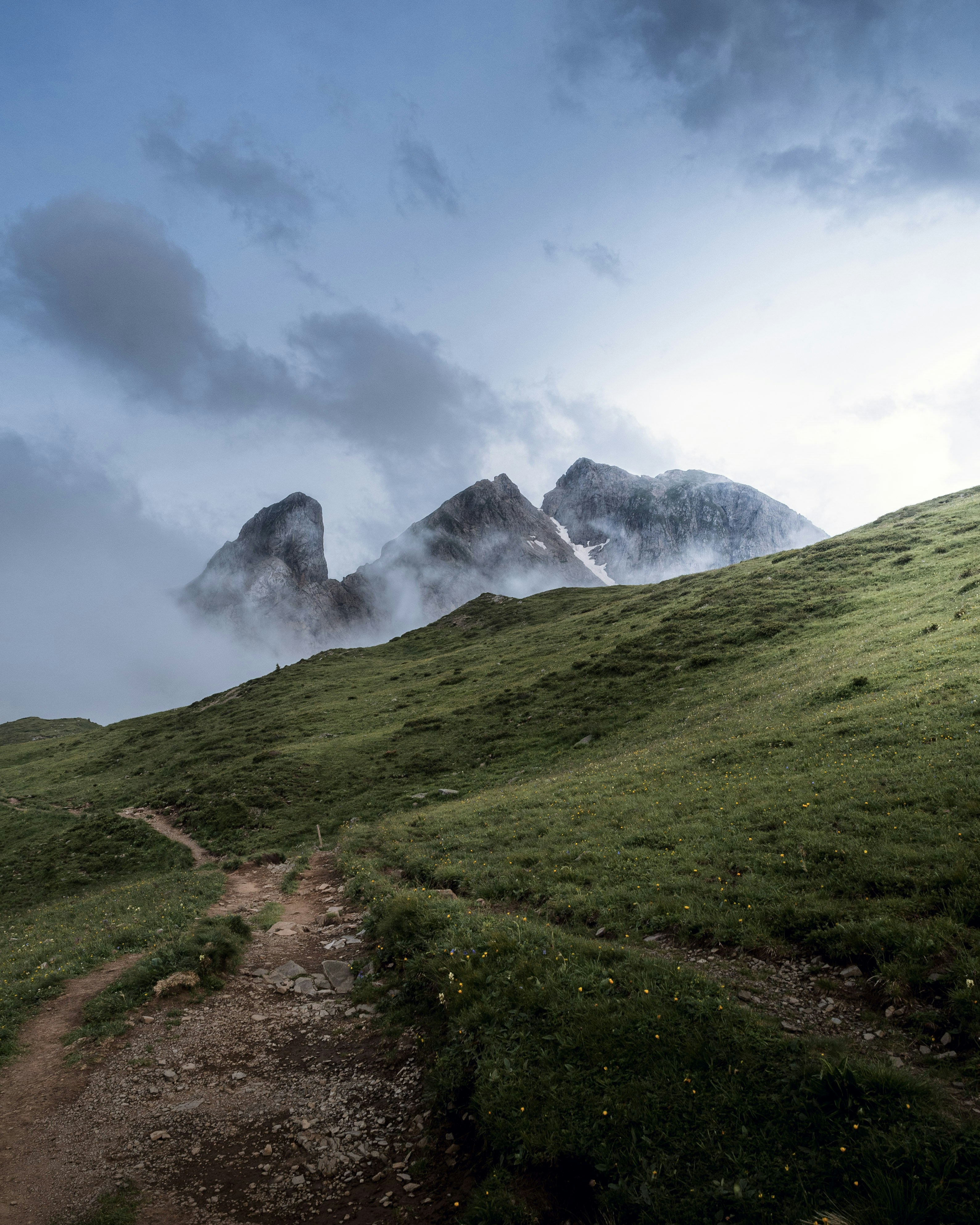 Un sendero que sube una colina cubierta de hierba con montañas al fondo