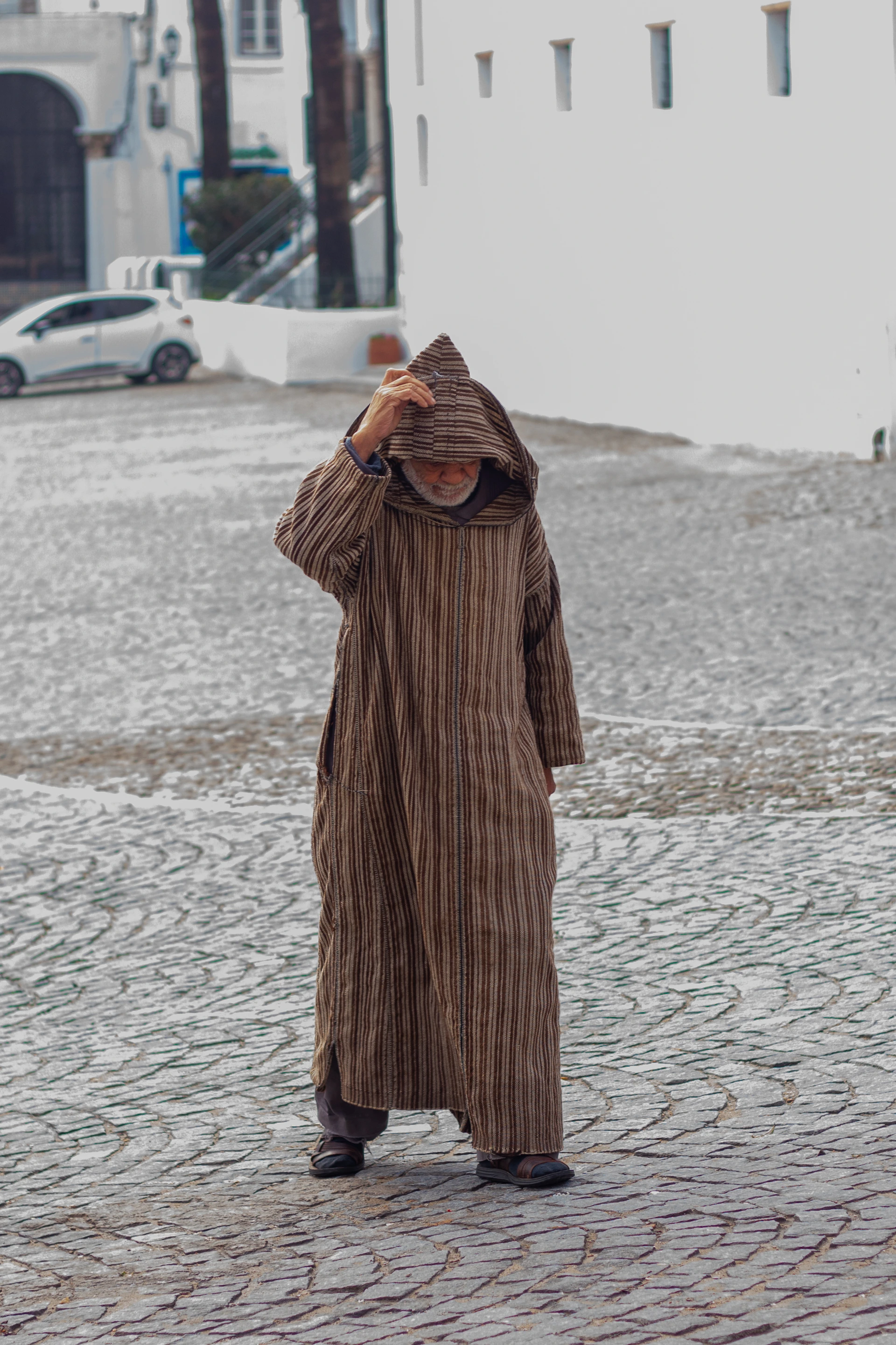 a man standing on a cobblestone street wearing a long coat