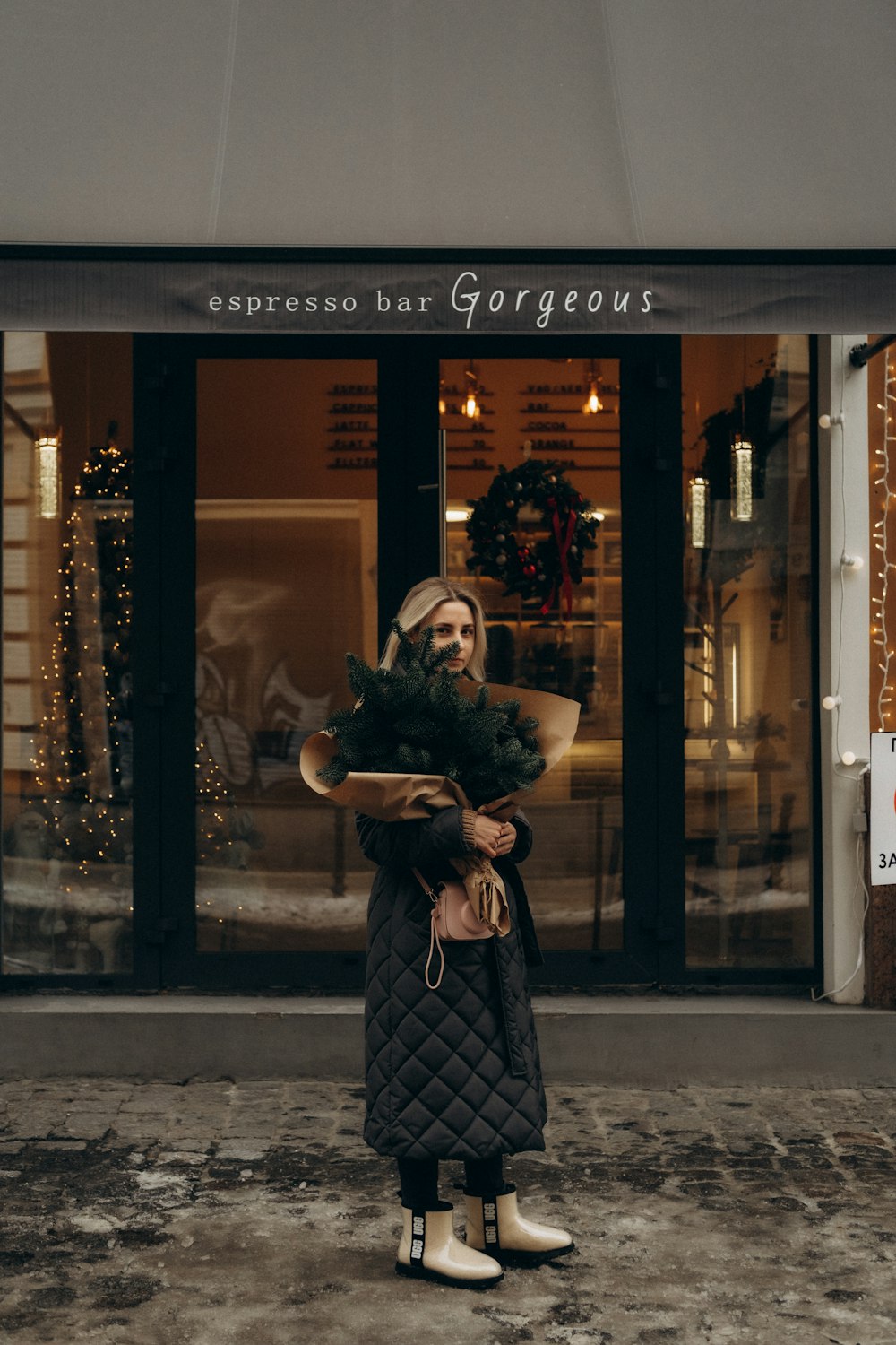 a woman standing in front of a store holding a christmas tree