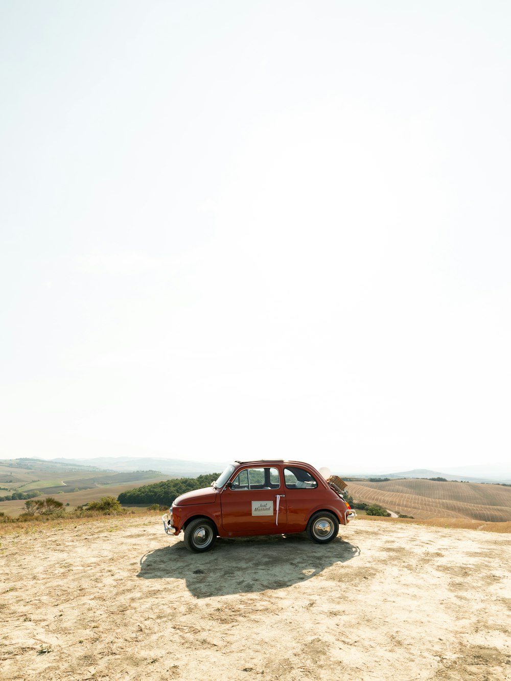 a small red car parked on top of a dirt field