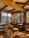 Cozy alpine refuge interior with wooden tables and mountain views through windows.