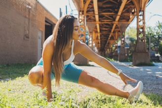 a woman stretching out in the grass in front of a bridge