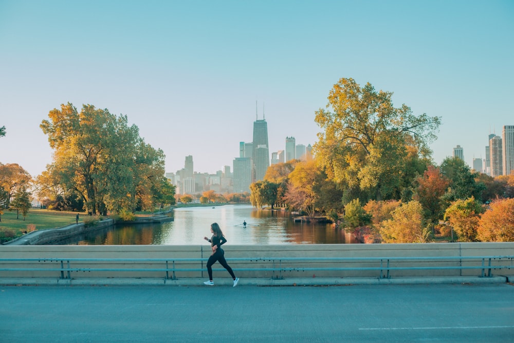 a woman running down a street next to a river