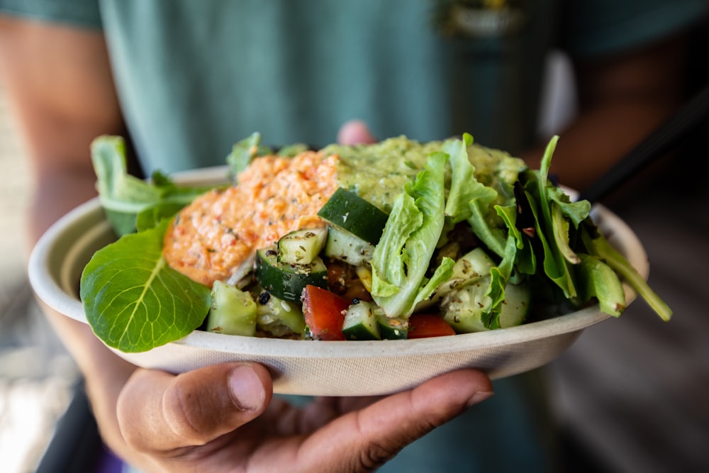 a person holding a bowl of salad with lettuce and tomatoes