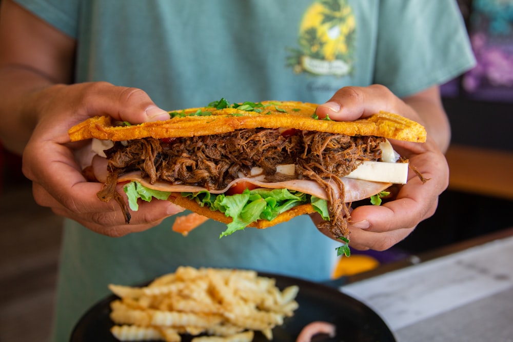 a person holding a sandwich with meat and lettuce