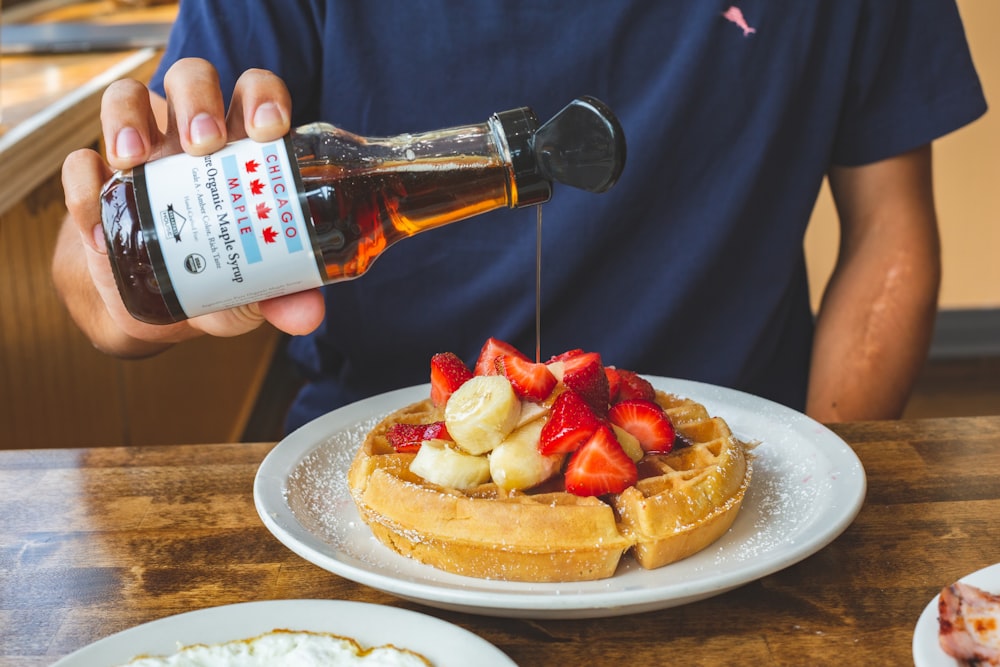 a person pouring syrup on a plate of waffles