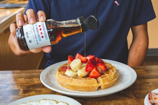 a person pouring syrup on a plate of waffles