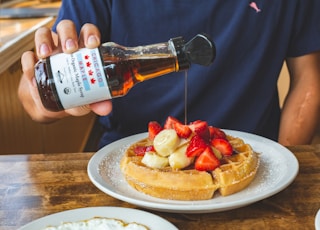 a person pouring syrup on a plate of waffles