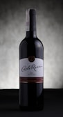 A bottle of Carlo Rossi red wine stands against a softly blurred, neutral background. The label prominently displays the brand name in elegant script, and the bottle is capped with a dark, sleek top.