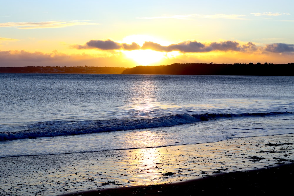 the sun is setting over the water at the beach