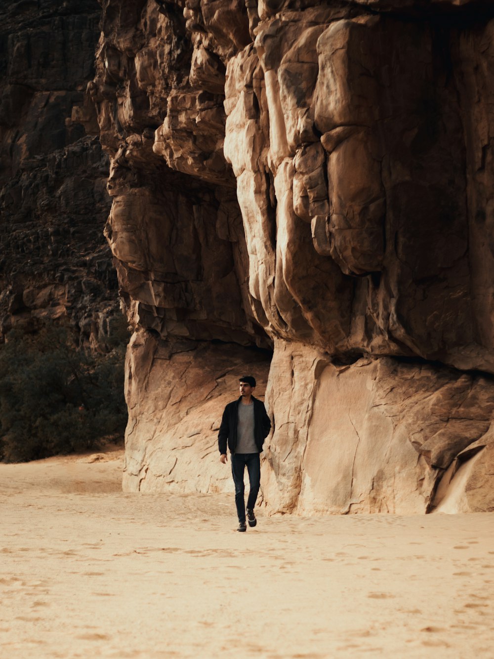 a man walking on a sandy beach next to a cliff