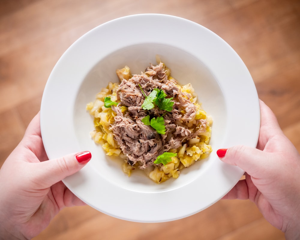 a person holding a plate of food on a wooden table