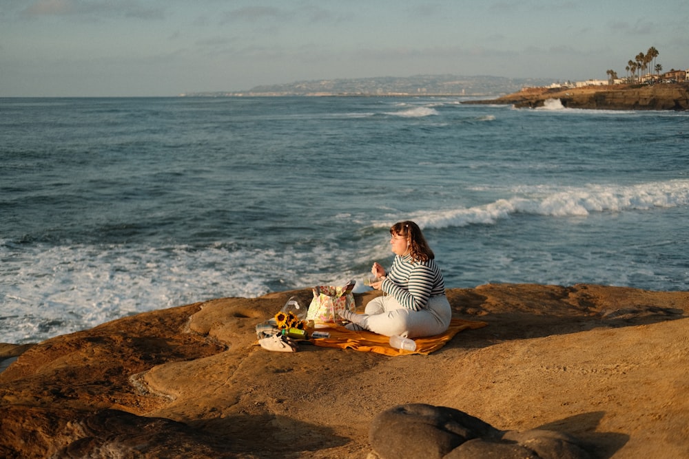 a woman sitting on top of a rock next to the ocean