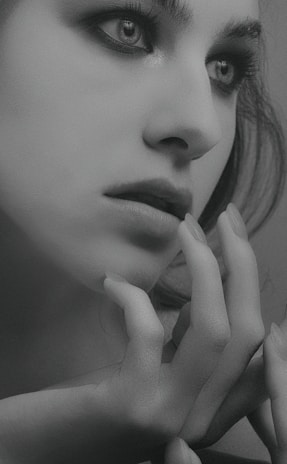 Black and white close-up of a model's intense gaze on the runway, highlighting dramatic makeup and sleek styling.