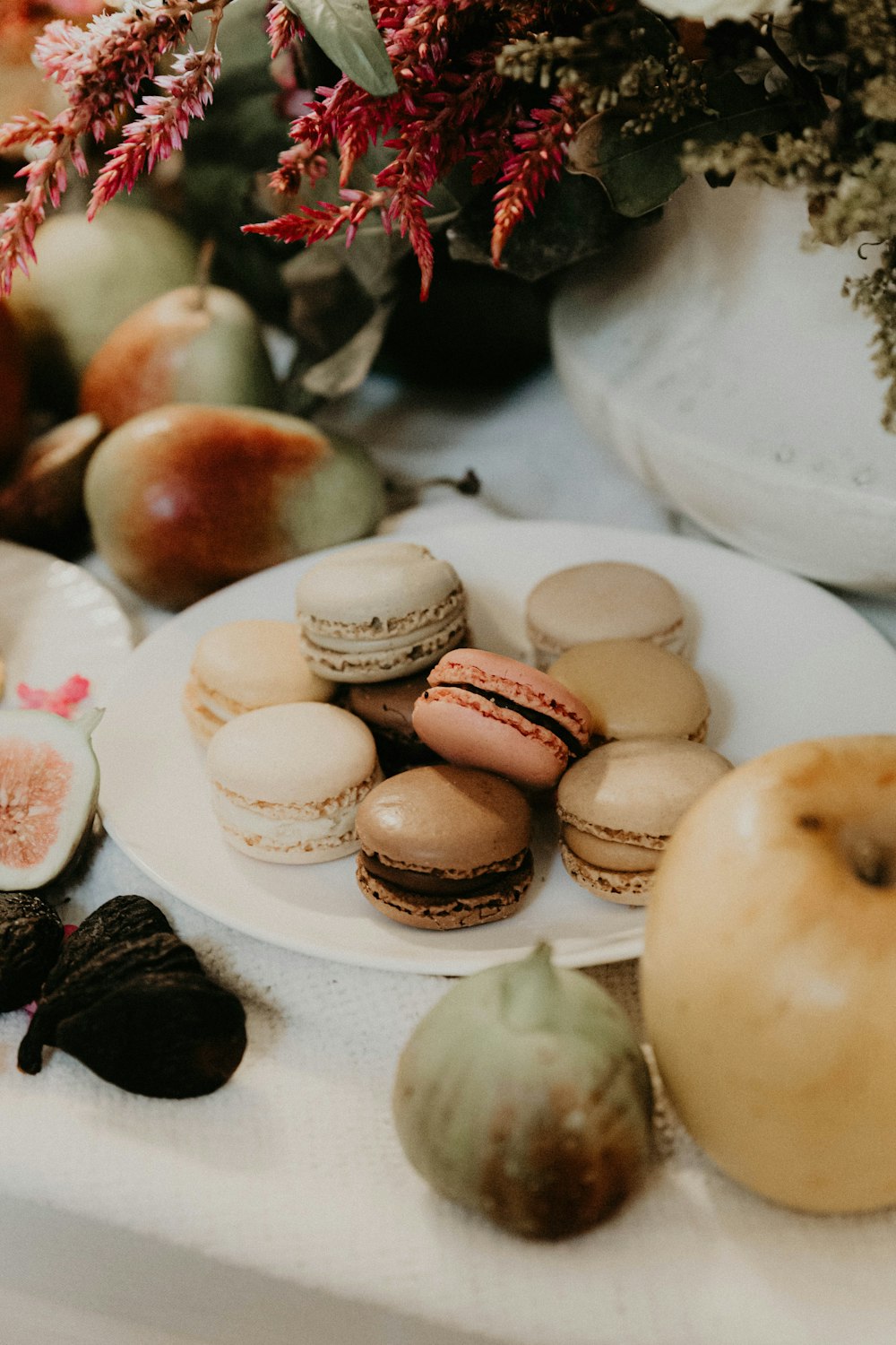 a table topped with a plate of macaroons next to a vase of flowers