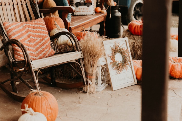 a porch with pumpkins, hay, and a rocking chair